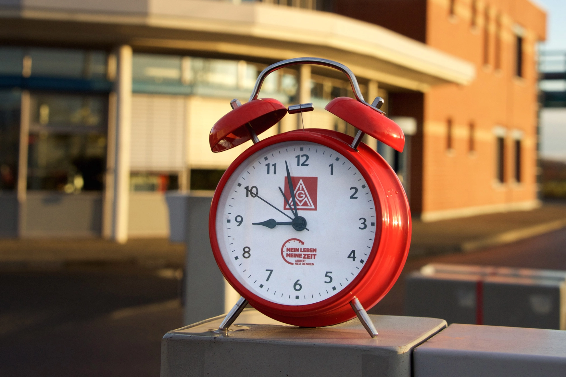 Ein roter Wecker vor einem Industriegebäude.