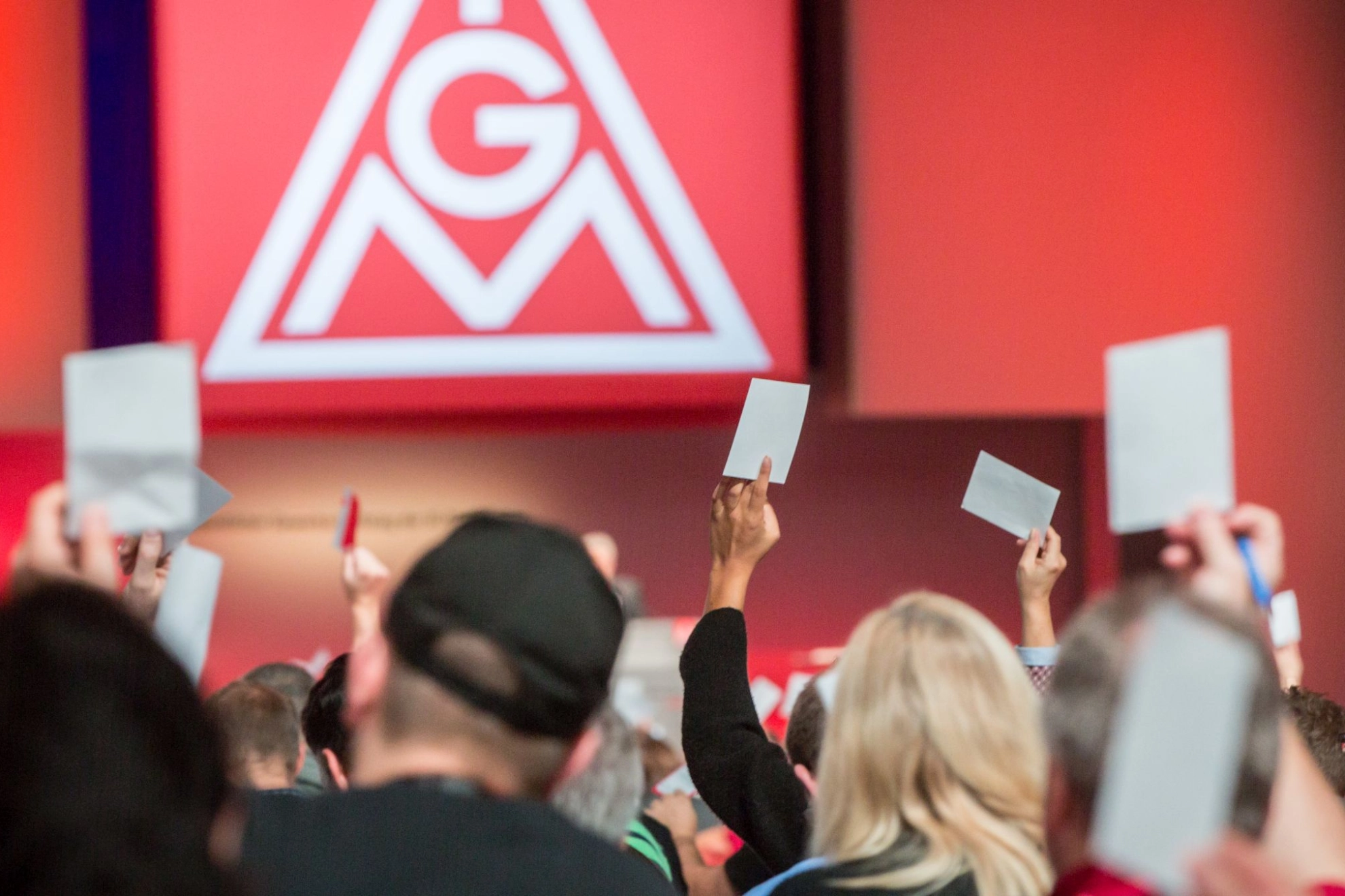 Delegierte auf dem Gewerkschaftstag 2015 der IG Metall bei einer Abstimmung, im Hintergrund das Logo der IG Metall